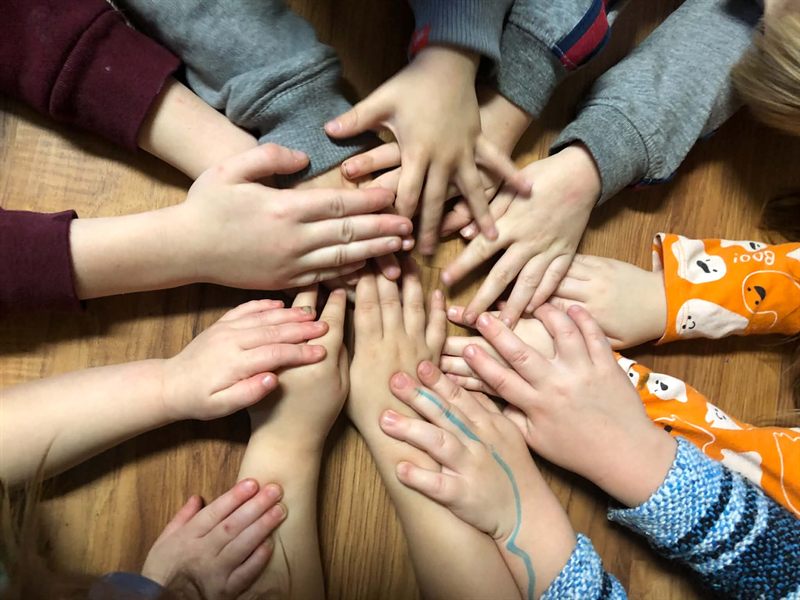 Children sitting in a circle with their hands stacked together in the middle